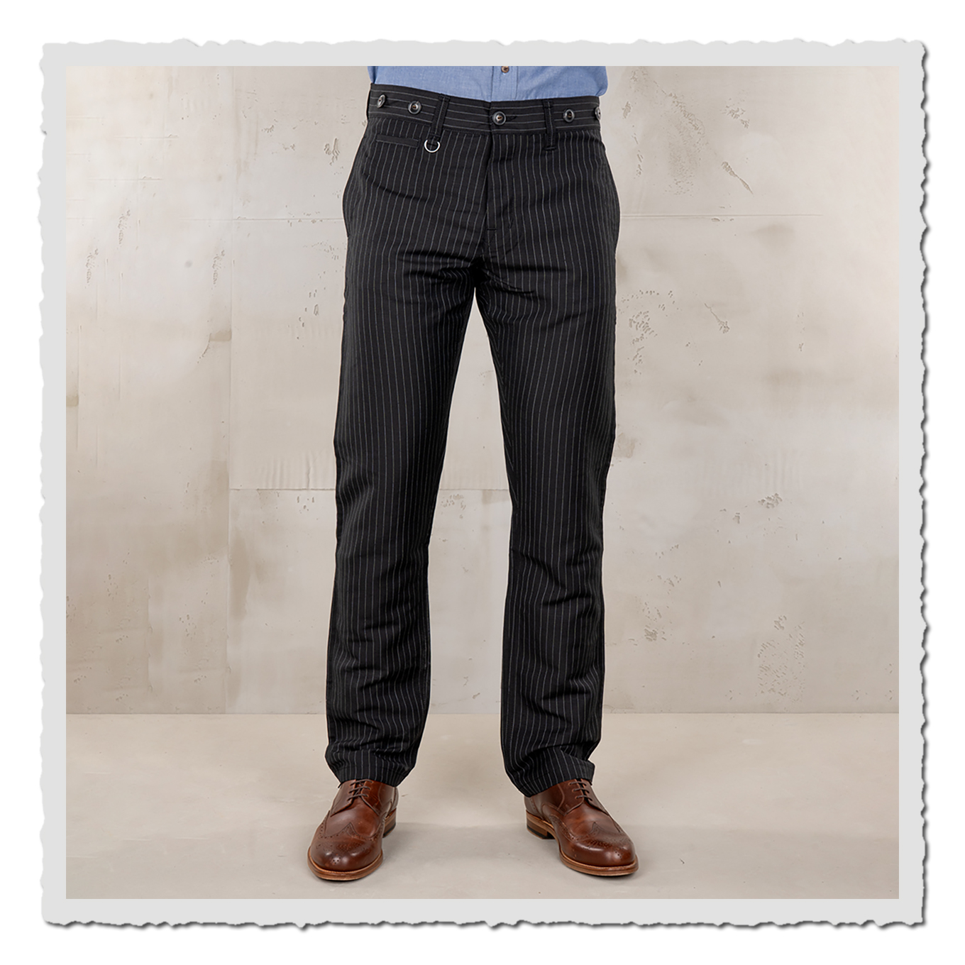 Model trägt schwarze Nadelstreifen-Hose, Frontansicht von Bund bis Schuhe, hellgrauer Studiohintergrund.